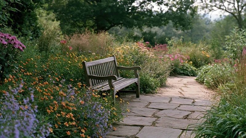 Wooden bench along a stone pathway surrounded by blooming flowers and greenery in a garden
