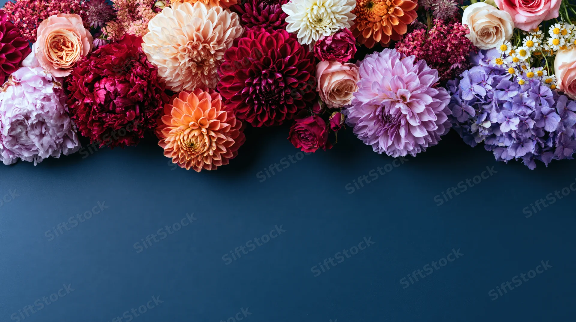 Mixed cut flowers arranged in a row along the top of a dark blue surface with copyspace below