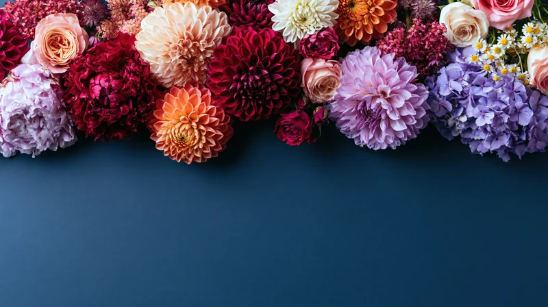 Mixed cut flowers arranged in a row along the top of a dark blue surface with copyspace below