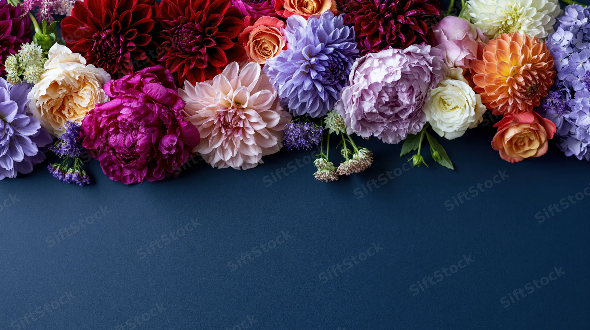 Flat lay of mixed cut flowers arranged along the top edge on dark blue surface with copyspace below