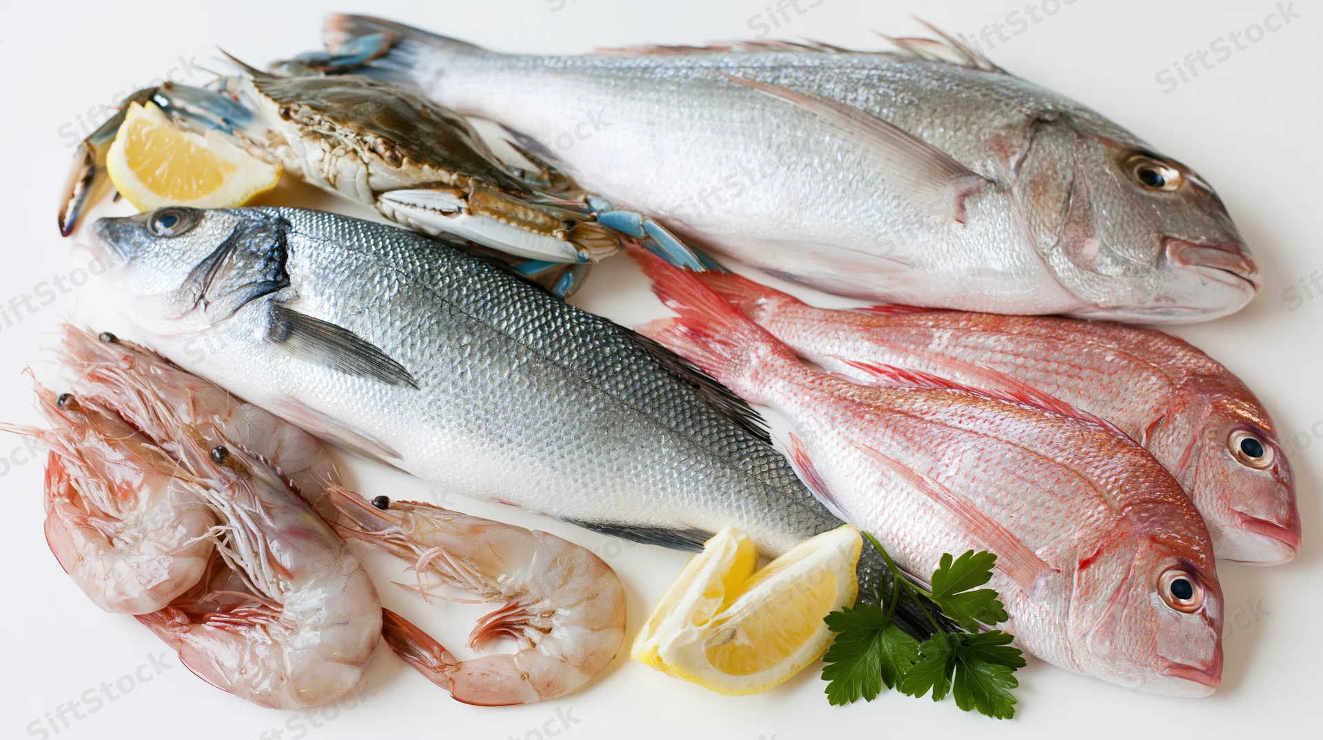 Fresh raw seafood assortment including fish shrimp crab and lemon on white surface