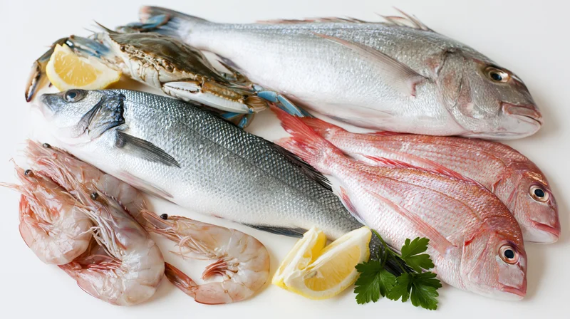 Fresh raw seafood assortment including fish shrimp crab and lemon on white surface