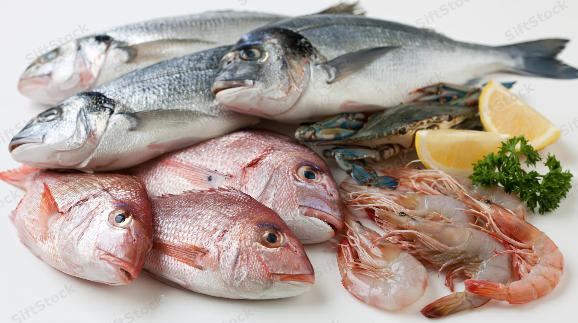 Fresh raw seafood assortment including fish shrimp crab and lemon on white surface