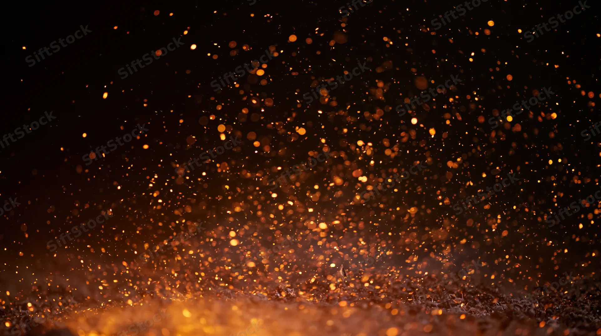 Glowing orange sparks rising from a dark surface against a black background