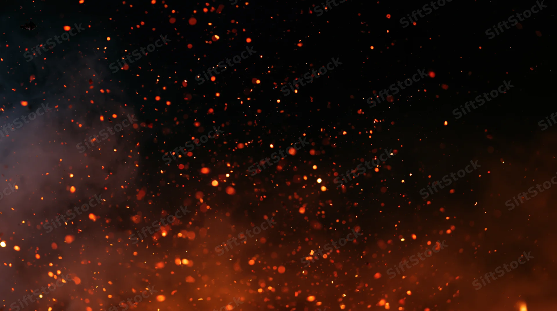 Glowing orange-red embers and sparks floating upward in dark night air with smoke