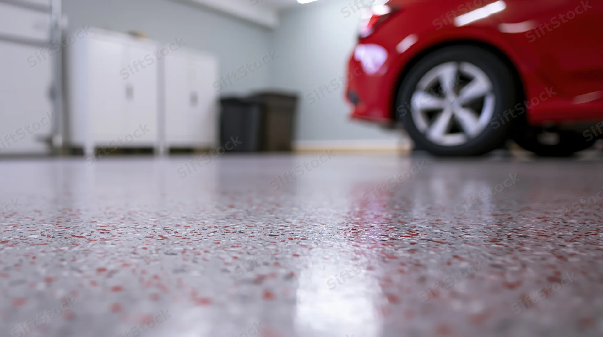 Polished epoxy garage floor with red car and white cabinets in background