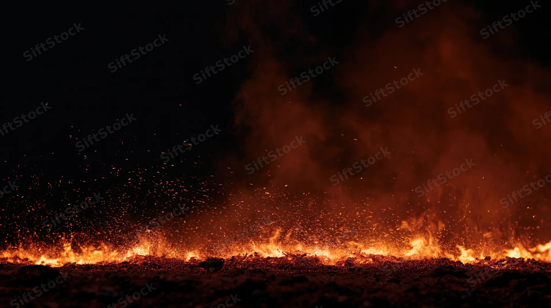 Low flames and flying embers burning along the ground at night