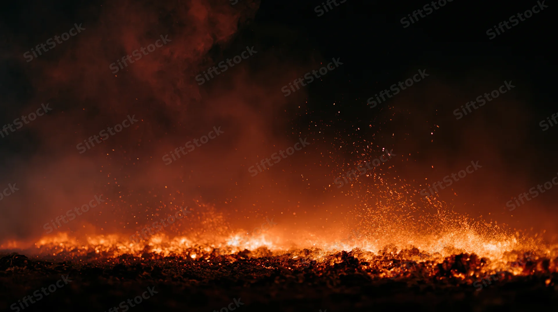 Low flames and flying embers burning along the ground at night