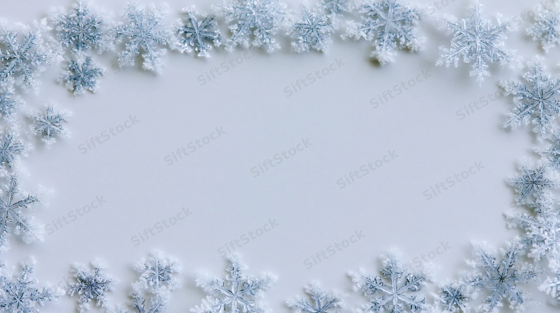 Snowflakes arranged in a border frame on a white surface with copyspace in the center