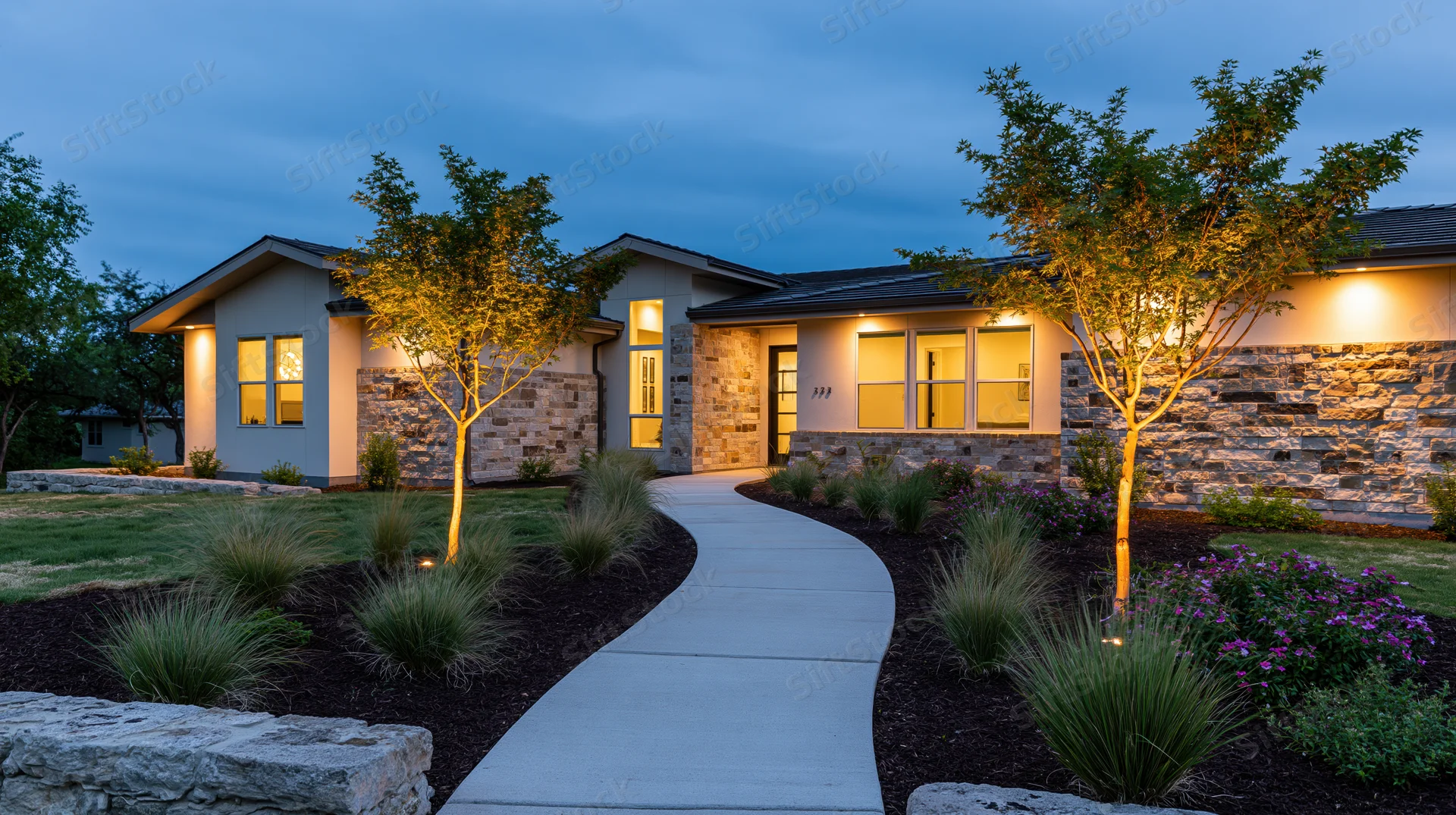 Modern single-story house exterior at dusk with curved concrete pathway and illuminated landscaping