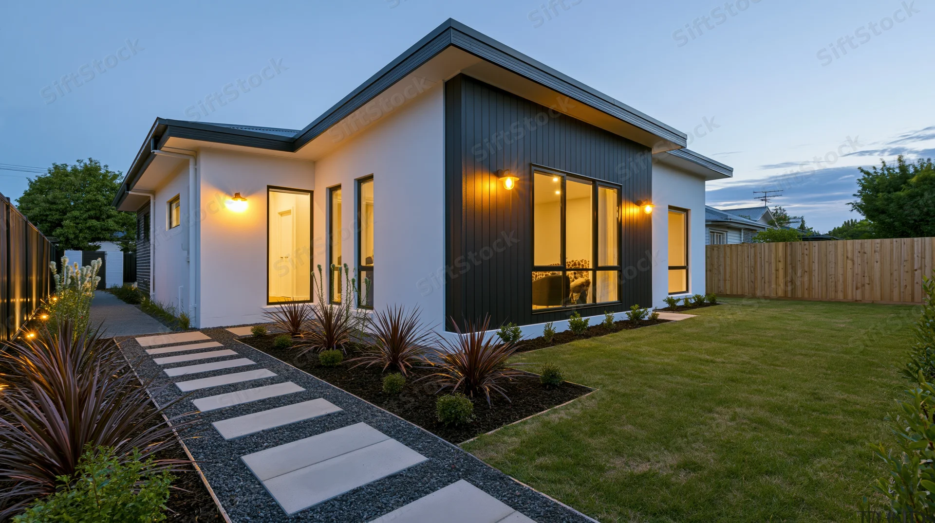 Modern suburban house exterior at dusk with illuminated windows, pathway, and landscaped front yard