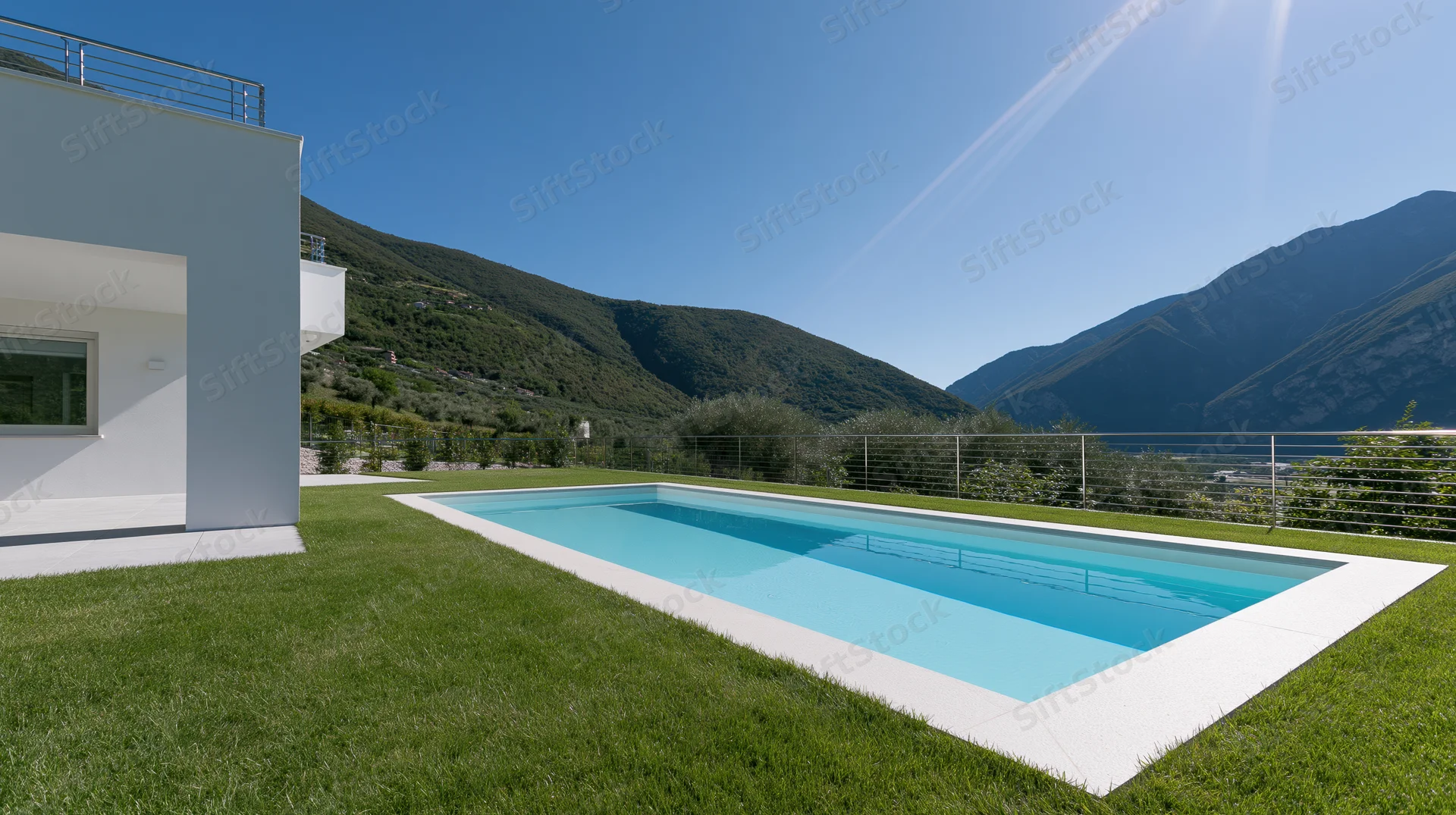 Modern white stucco villa exterior with rectangular swimming pool on grassy lawn overlooking mountains