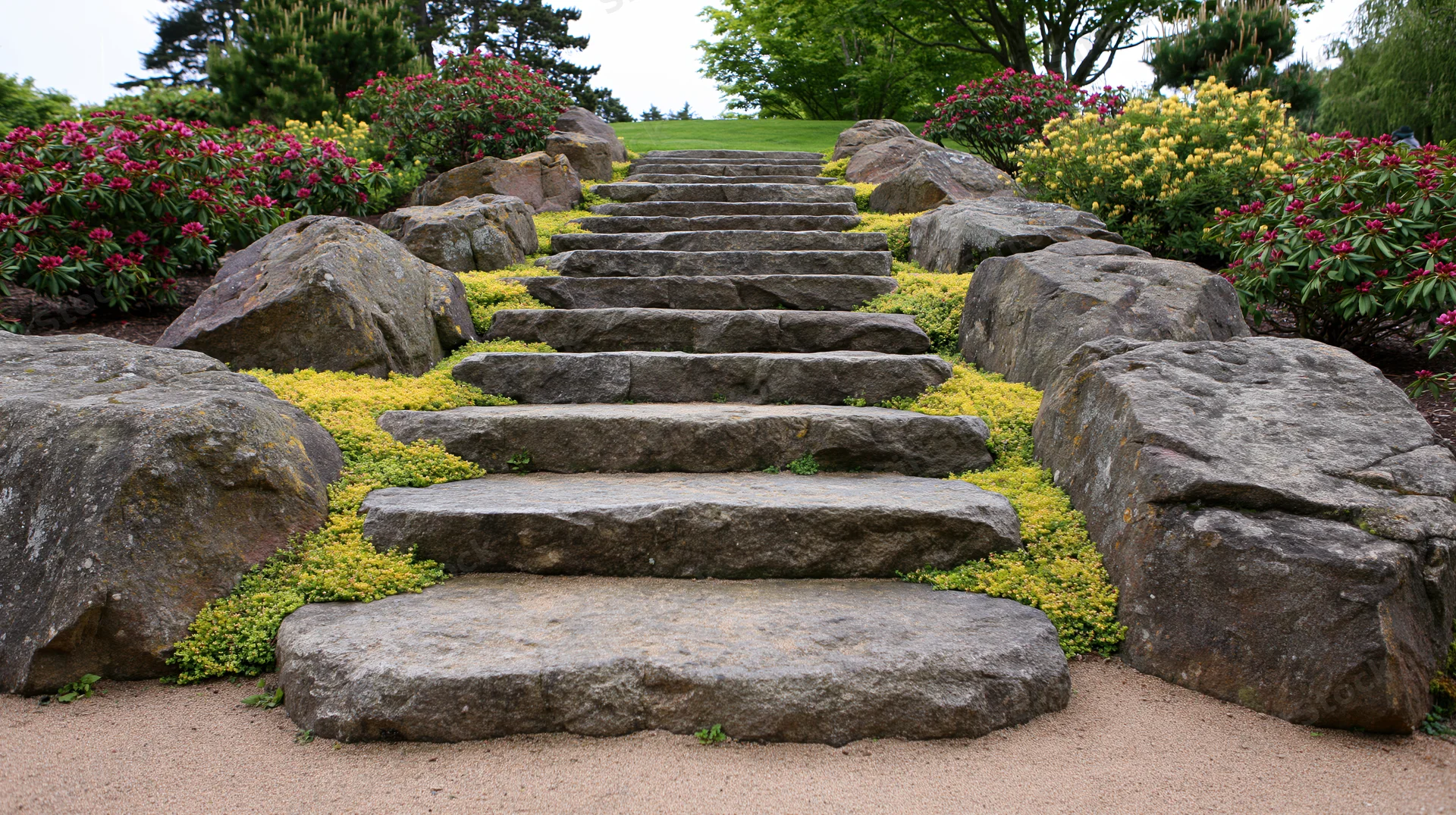 Stone staircase ascending through a landscaped garden with flowering shrubs and rocks