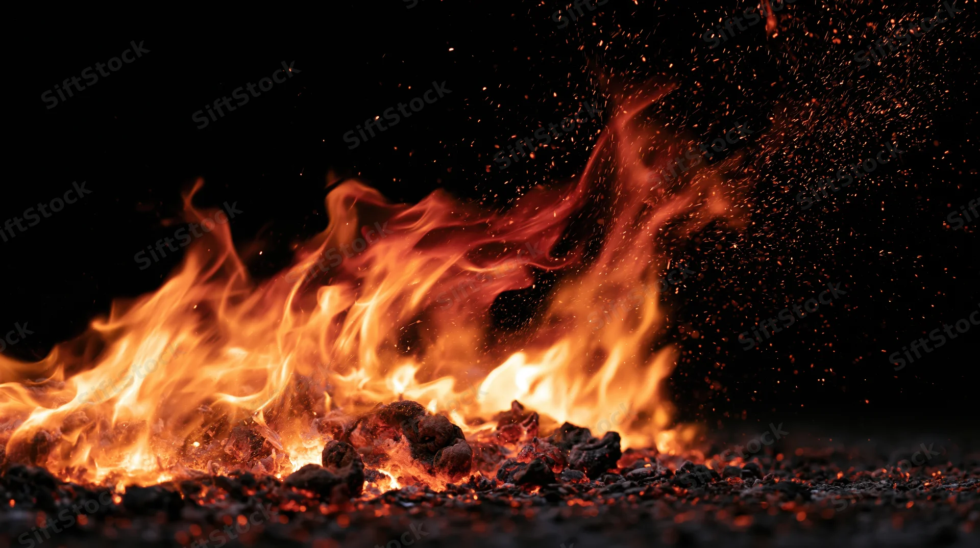 Flames burning intensely with sparks and glowing embers against a black background