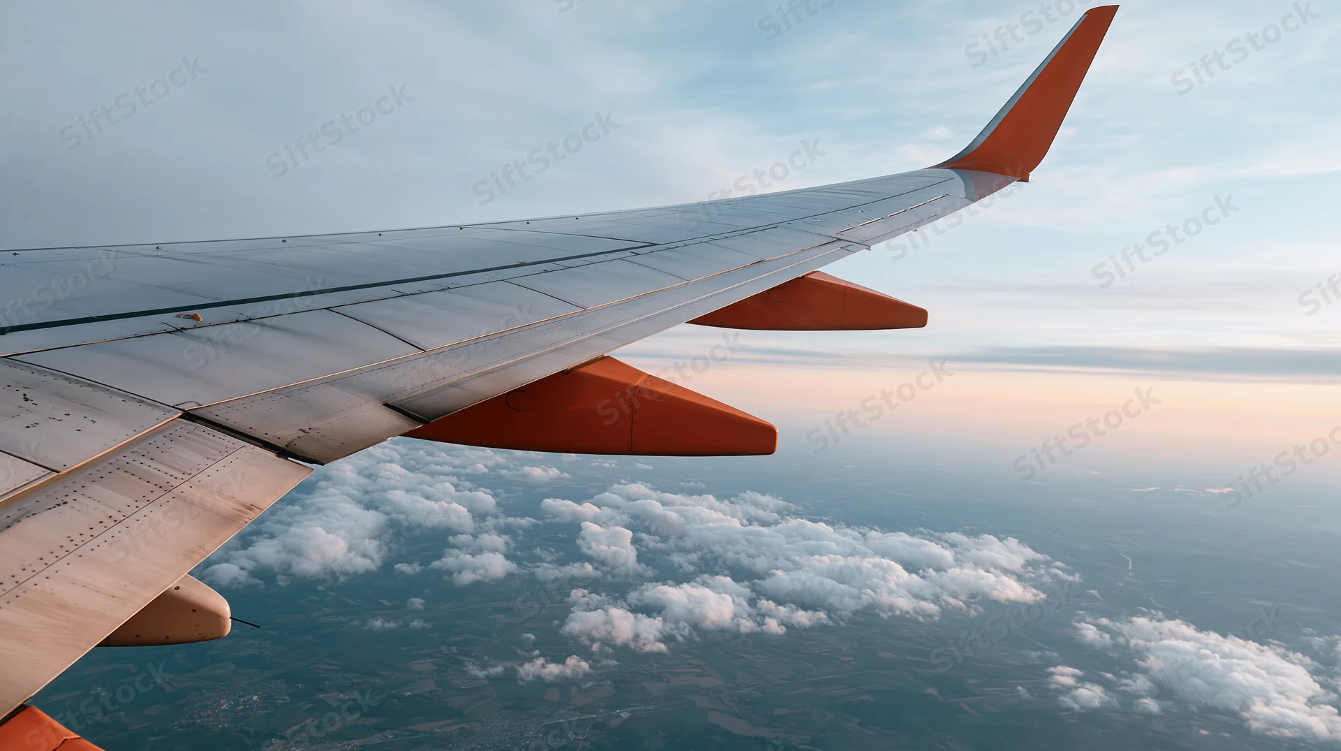 Airplane wing extending over clouds and landscape viewed from passenger window during flight