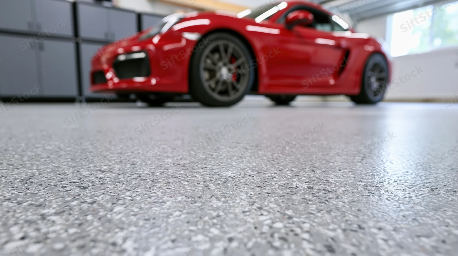 Red sports car parked in a clean residential garage viewed from low angle near the floor