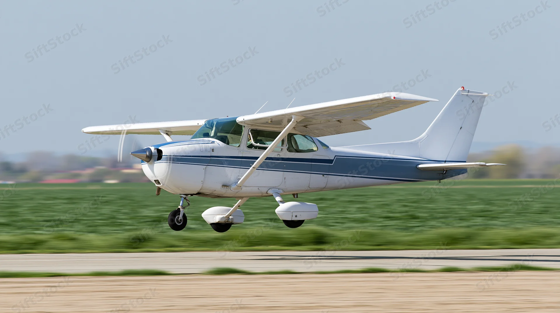 Small white and blue single-engine aircraft landing on a runway with green field in background