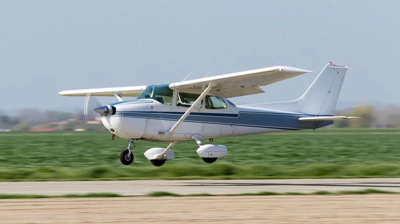 Small white and blue single-engine aircraft landing on a runway with green field in background