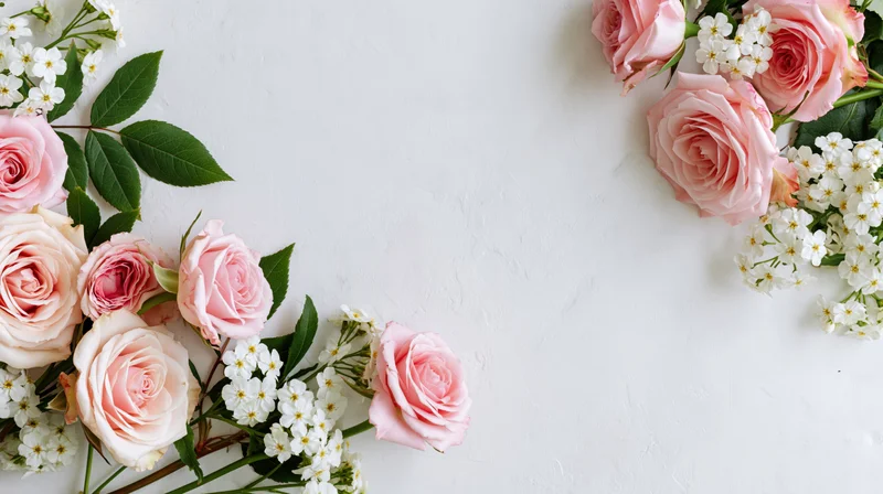 Pink roses and white blossoms arranged along the edges of a white surface