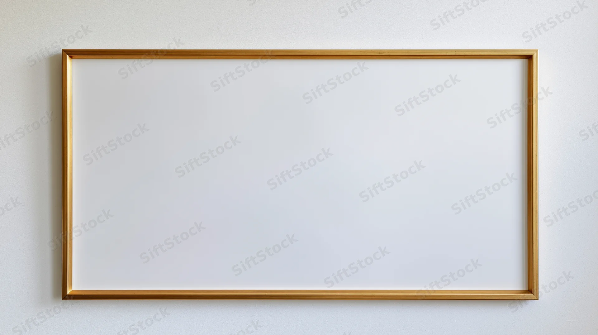 Thin gold metal picture frame with empty white interior hanging on a plain wall