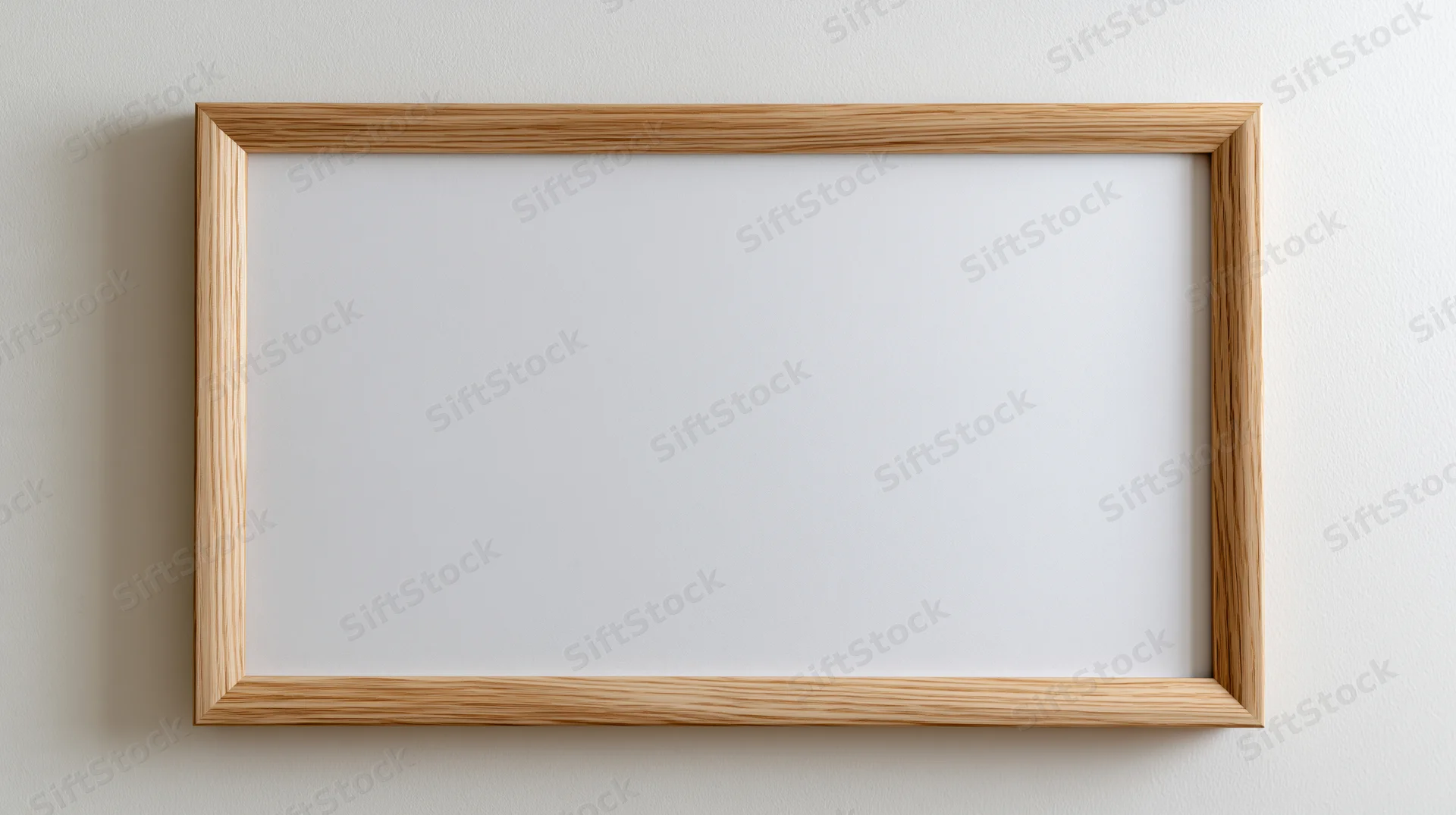 Light oak wooden picture frame with blank white interior hanging on a wall