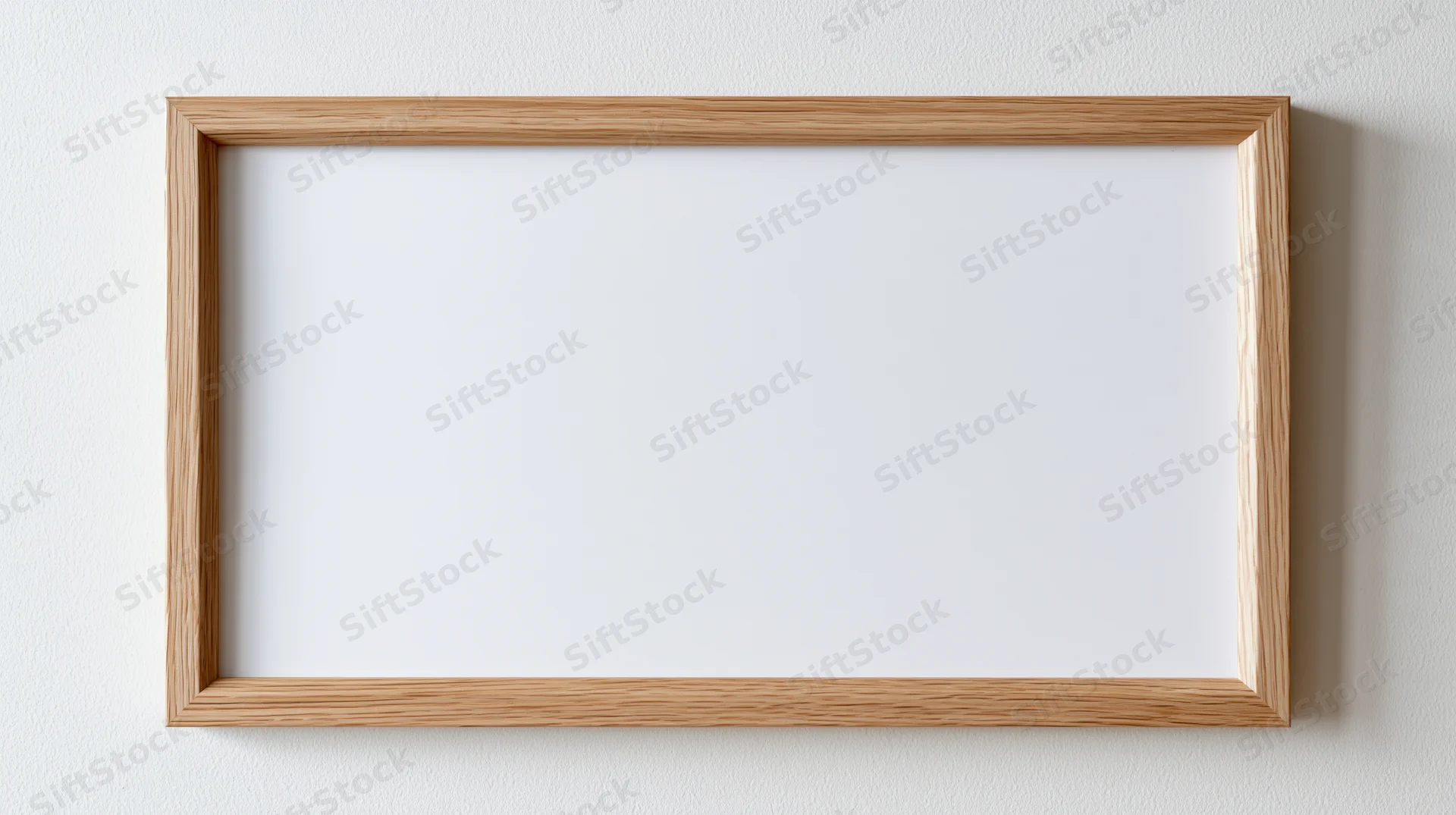 Light oak wooden picture frame with blank white interior hanging on a white wall