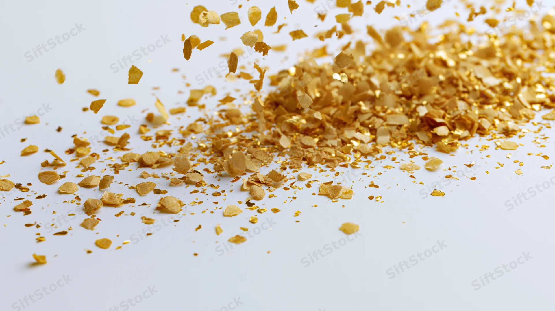 Gold confetti pieces scattered across a white surface with some in motion