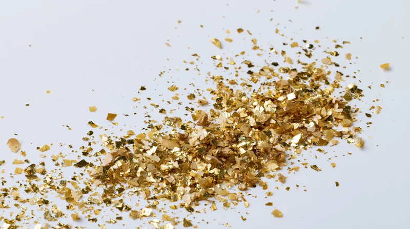 Scattered gold confetti and metallic flakes on a white surface