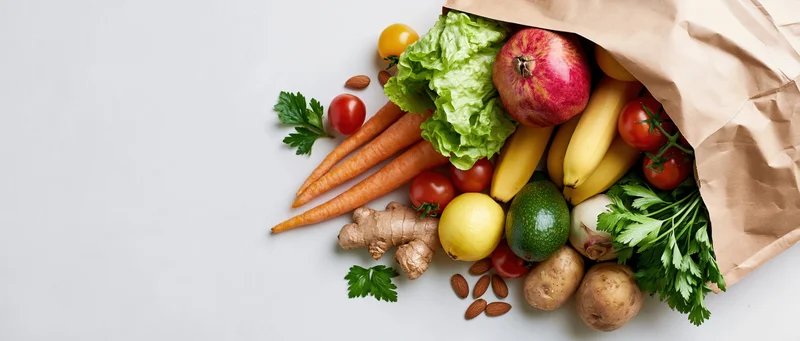 Brown paper bag tipped over spilling fresh fruits and vegetables on white surface