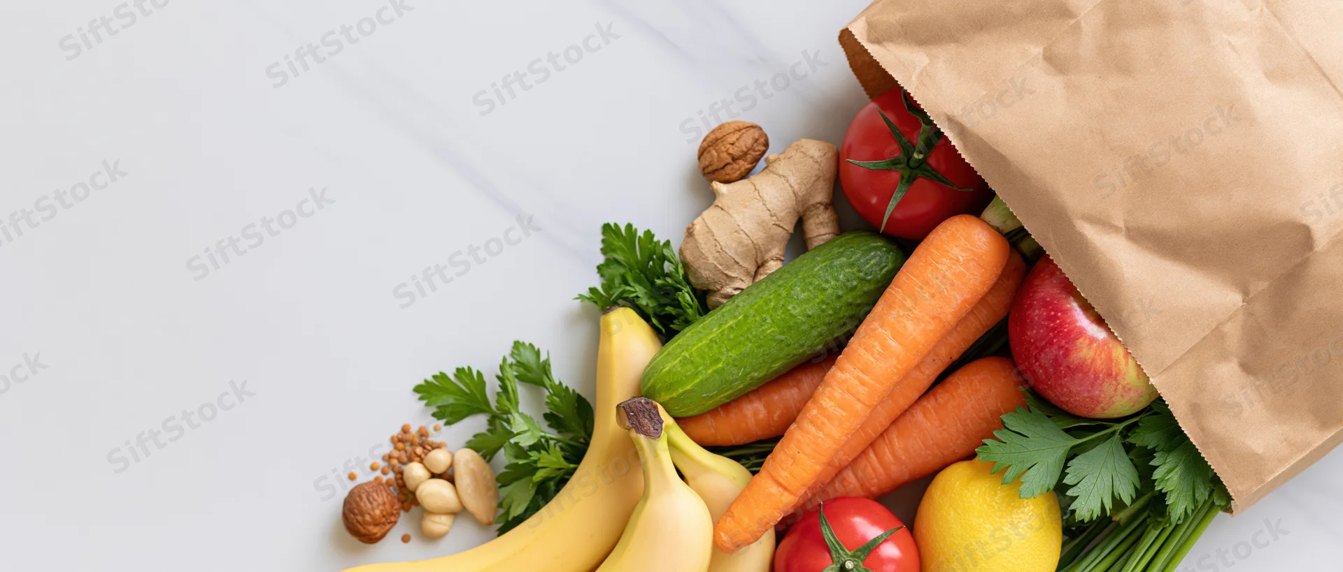 Brown paper grocery bag tipped over spilling fresh vegetables and fruits on white marble surface