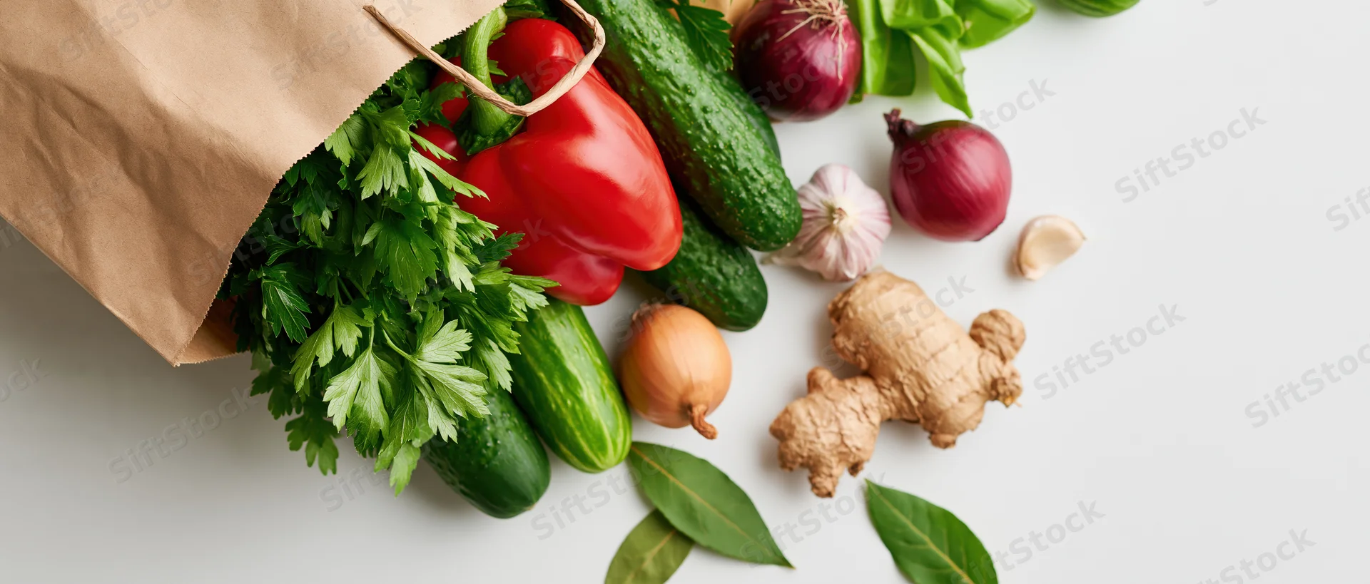 Brown paper bag spilling fresh vegetables and herbs on white surface