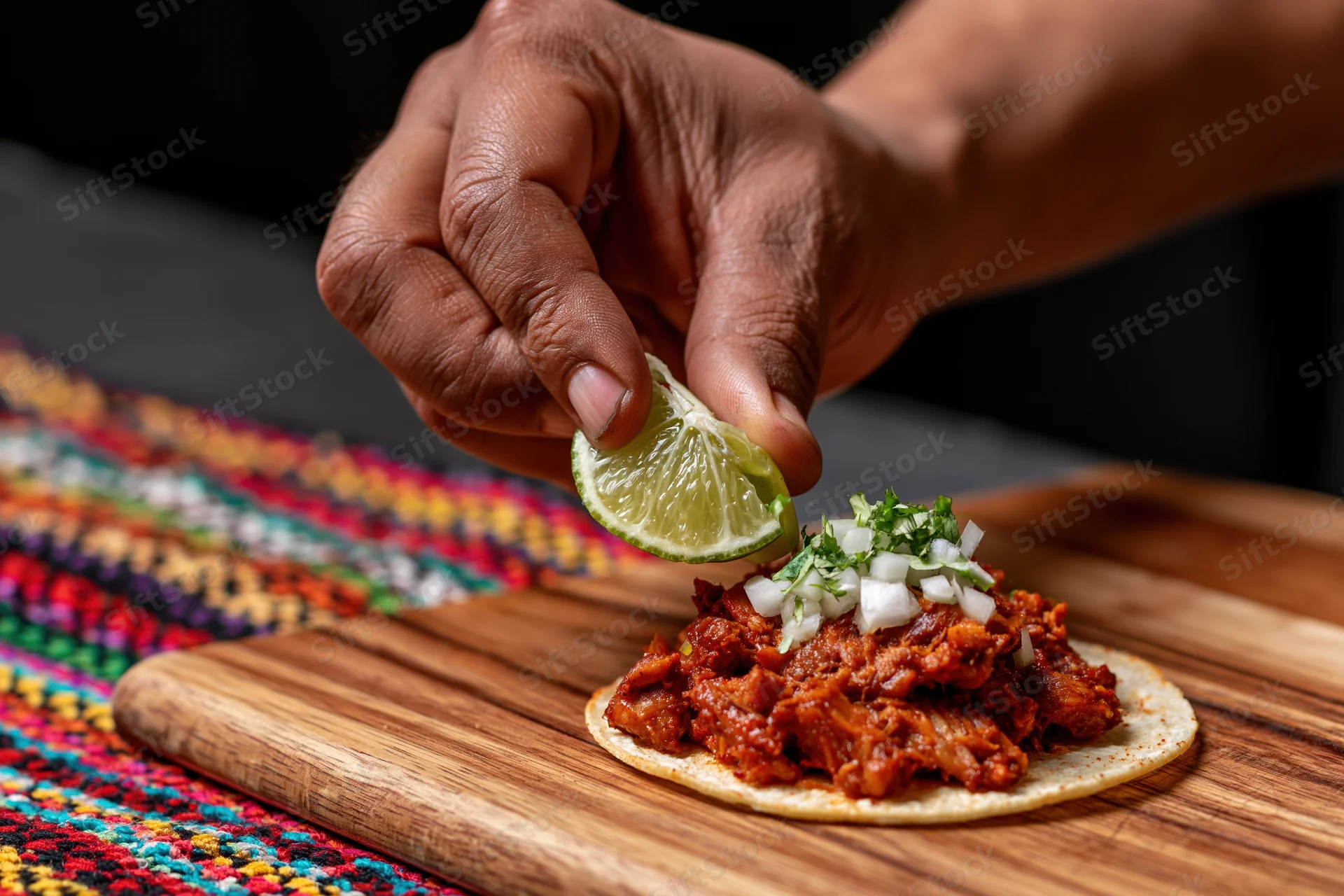 Hand squeezing lime over taco al pastor on wooden board with colorful textile beneath