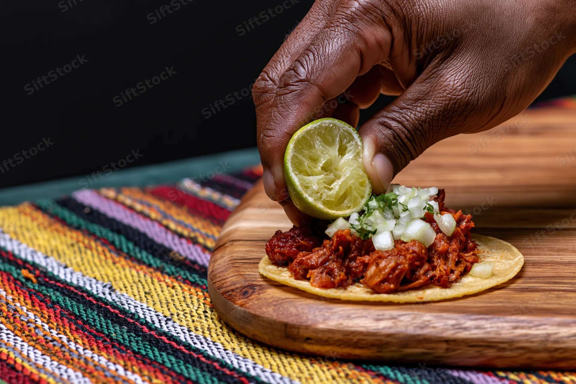 Hand squeezing lime over taco with meat and onions on wooden plate