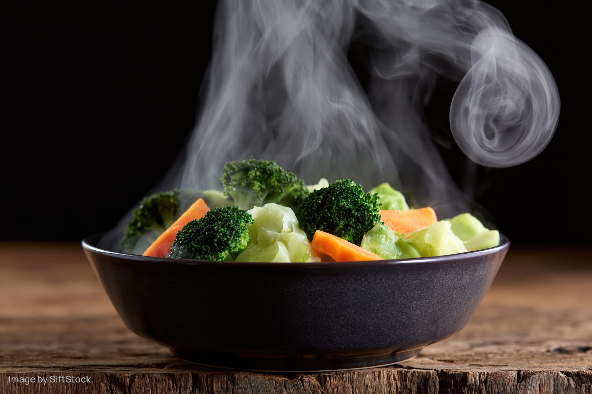 Steamed mixed vegetables in a dark ceramic bowl on a wooden table