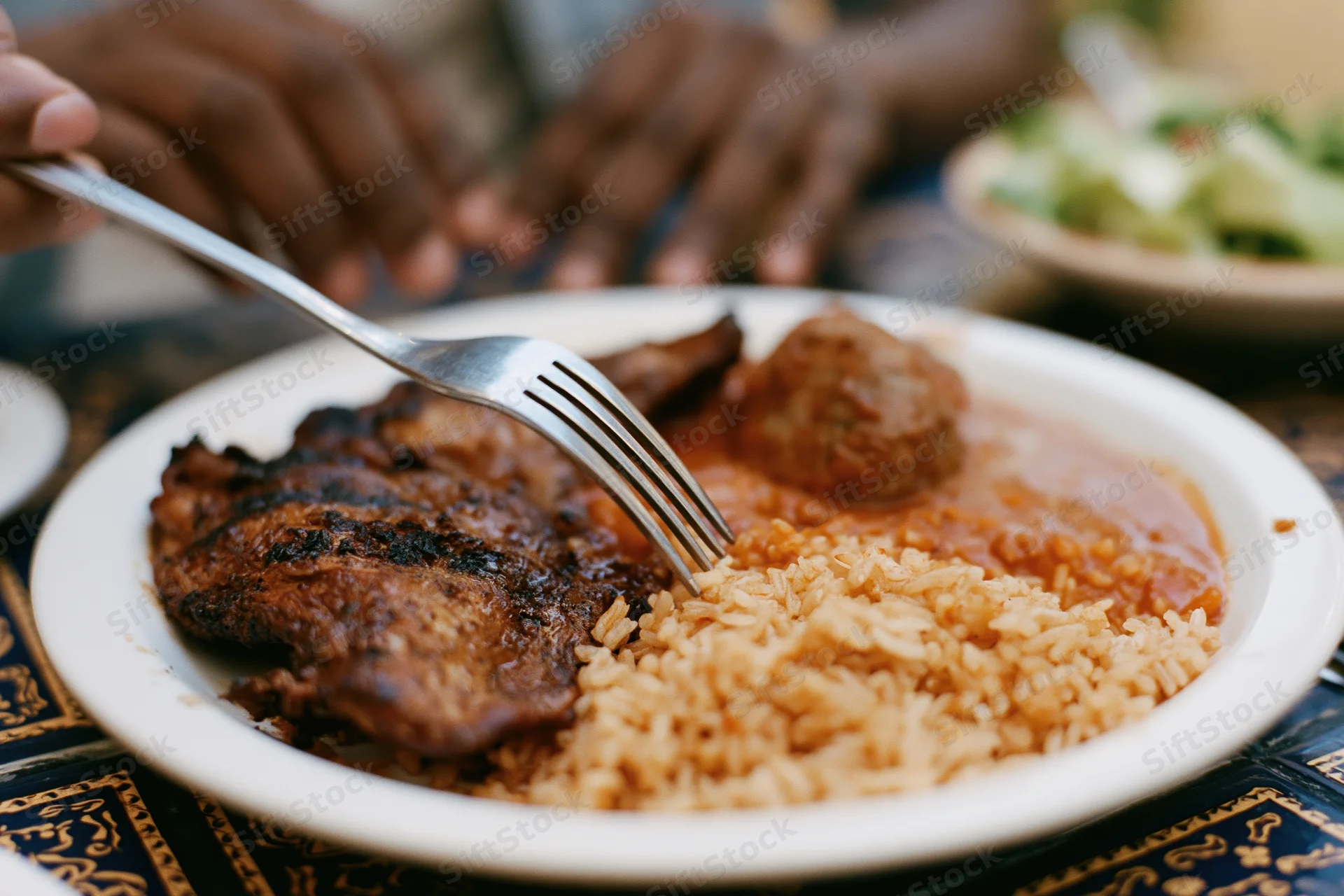 Fork pressing into grilled chicken and rice on a plate at a dining table