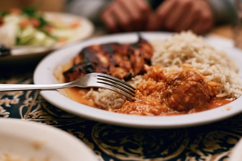 Fork pressing into grilled chicken and rice on a patterned tablecloth