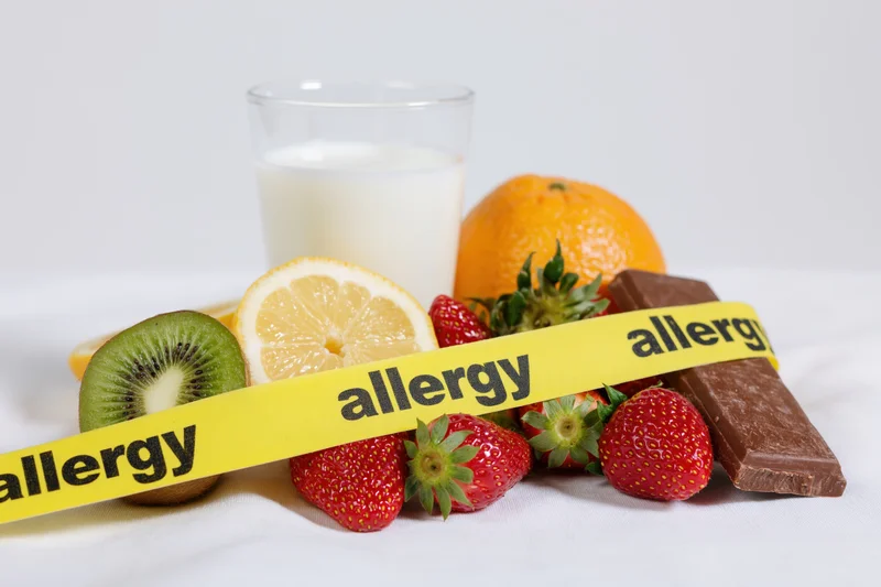 Yellow allergy tape across milk and fresh fruits on white surface