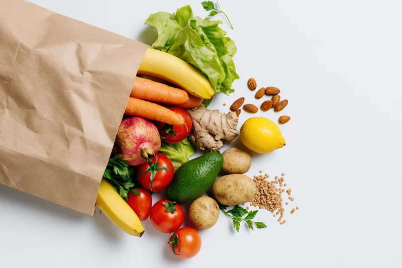 Kraft paper grocery bag tipped on its side with fresh produce spilling out onto white surface