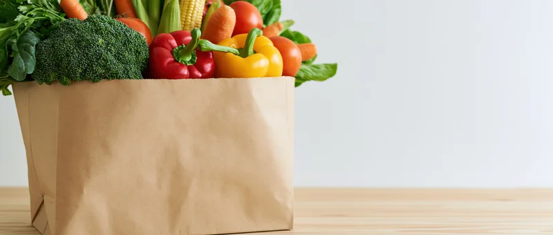 Kraft paper bag overflowing with fresh vegetables on wooden table