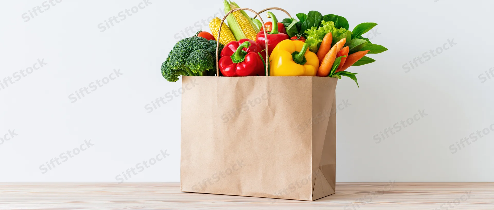 Kraft paper bag filled with fresh vegetables on wooden surface