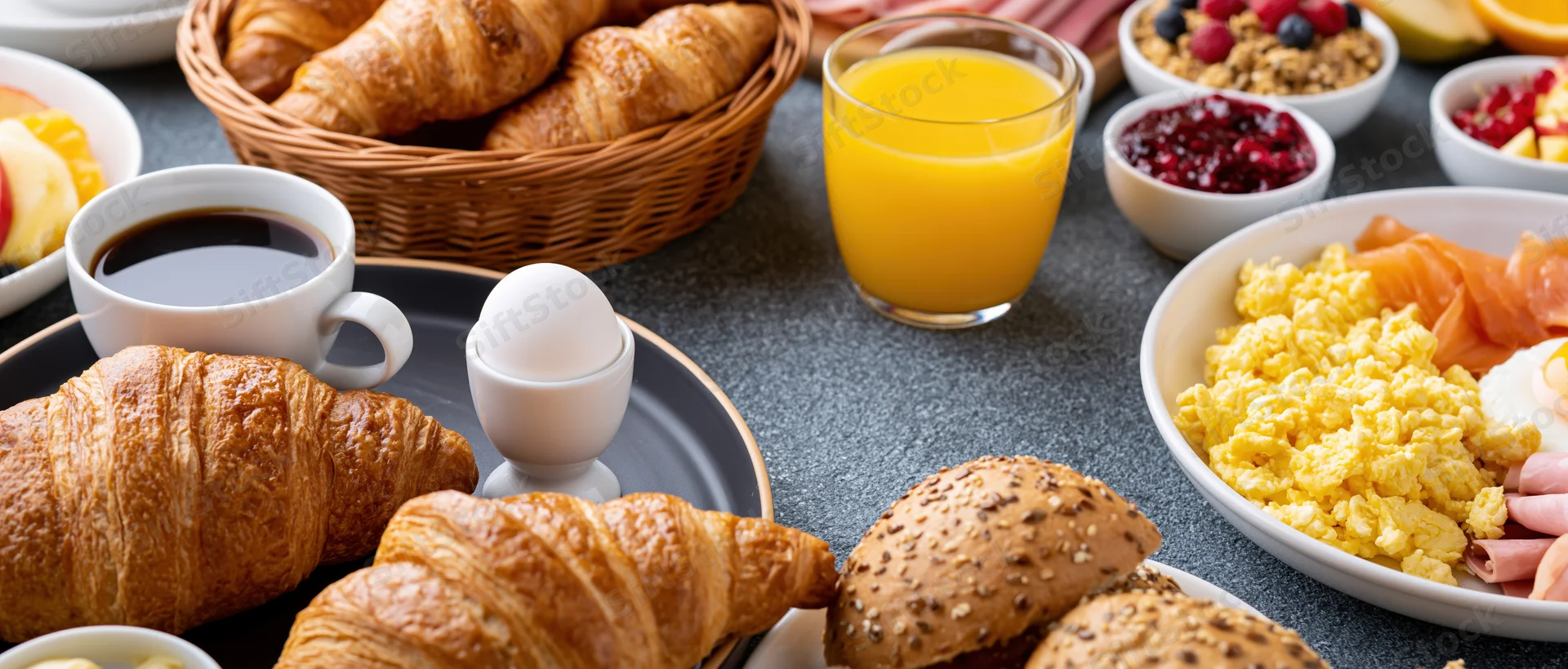 Continental breakfast spread on a table with croissants, eggs, orange juice, coffee, and assorted foods