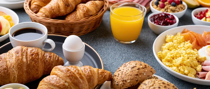 Continental breakfast spread on a table with croissants, eggs, orange juice, coffee, and assorted foods