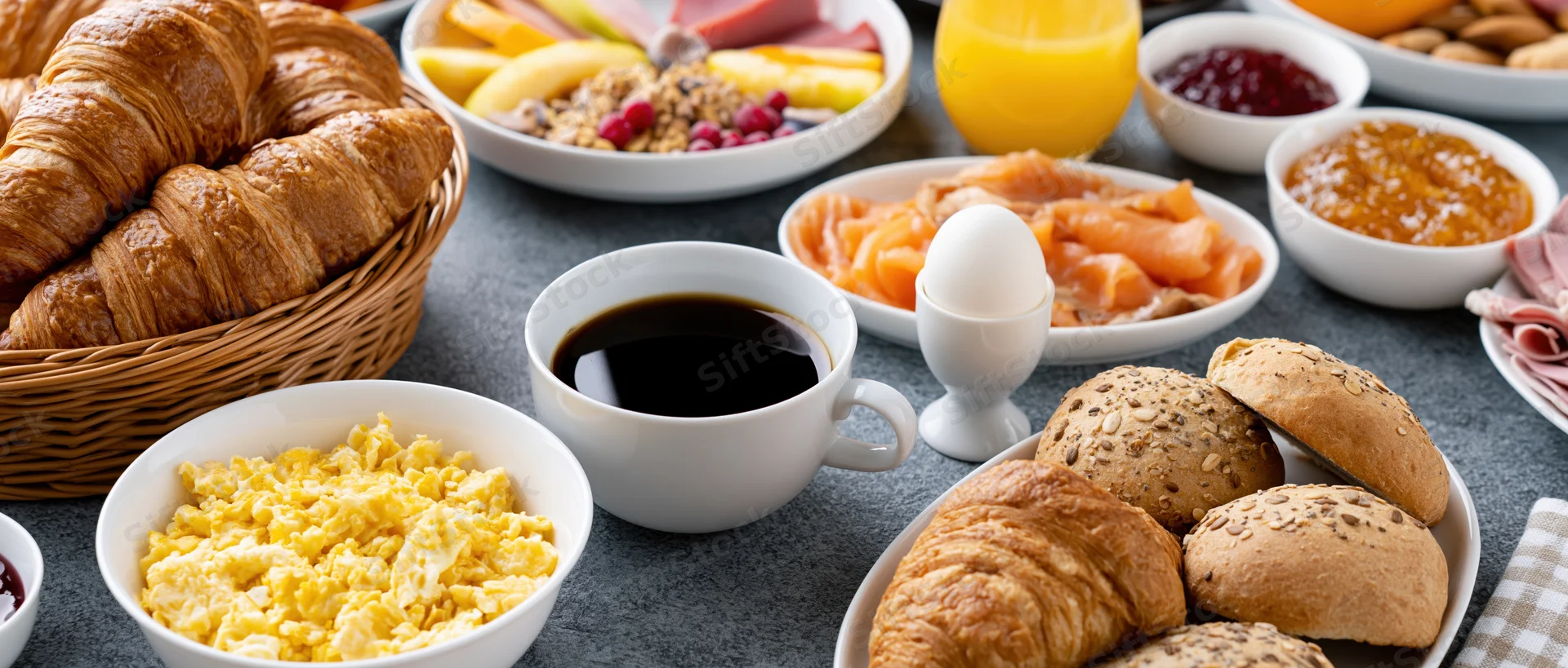 Continental breakfast spread on a table with croissants, coffee, eggs, salmon, yogurt, and jam