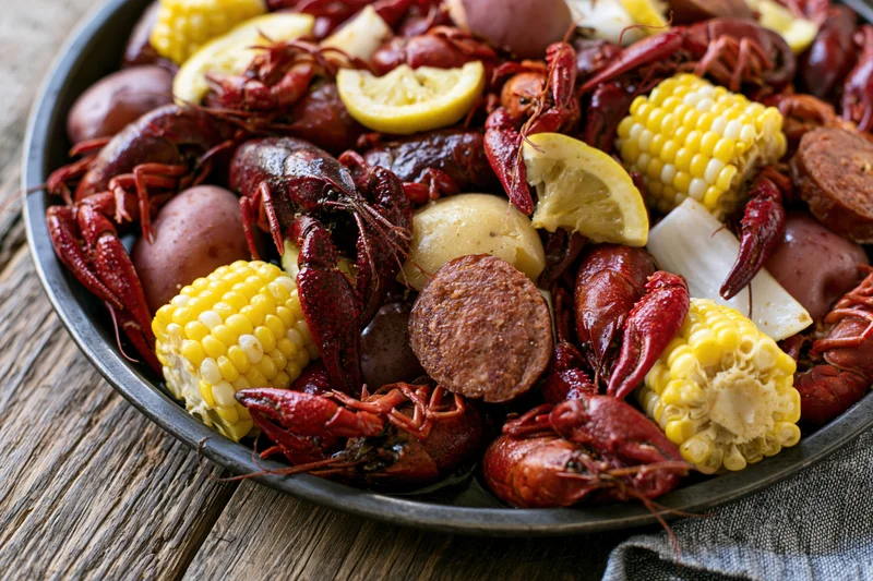 Crawfish boil served in a metal tray with corn, potatoes, sausage and lemon on a wooden table