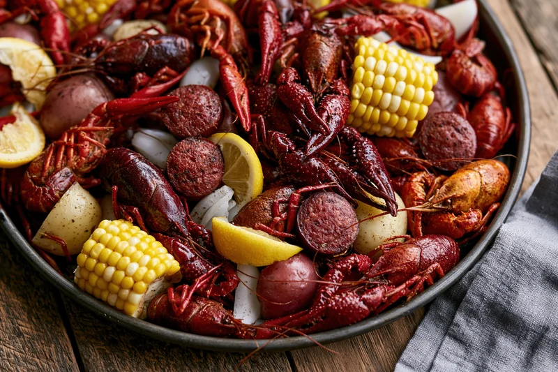Crawfish boil served in a dark metal tray with corn, potatoes, sausage, and lemon on a wooden table