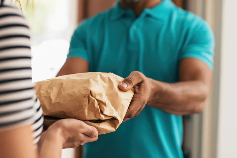 Delivery worker handing paper food bag to customer at door