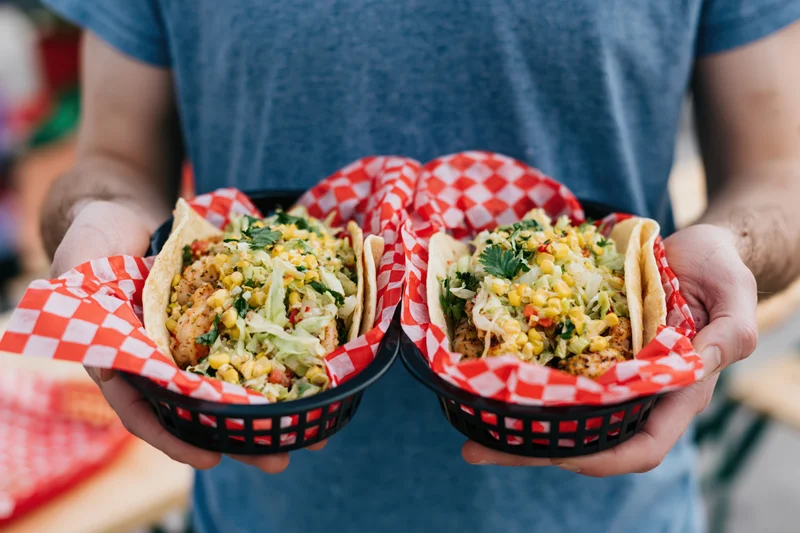 Man holding two baskets of loaded shrimp tacos with checkered paper lining