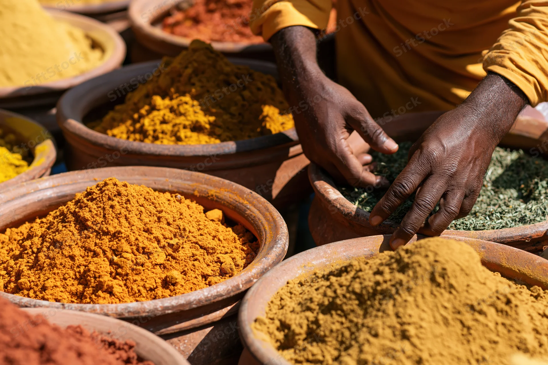 Vendor arranging dried spices and herbs in clay bowls at an outdoor market