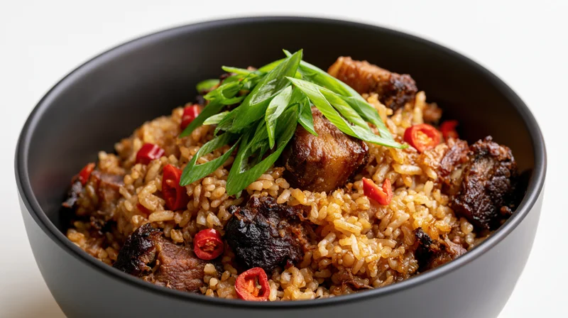 Fried rice with pork chunks and green onions in a black ceramic bowl