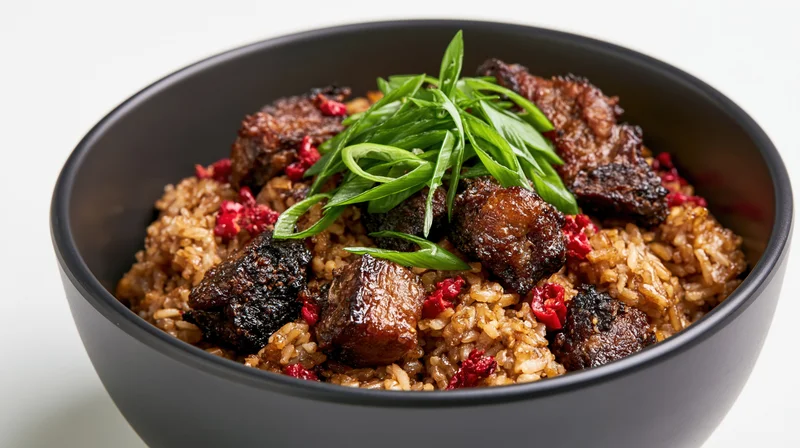 Fried rice with pork chunks and green onions in a black ceramic bowl